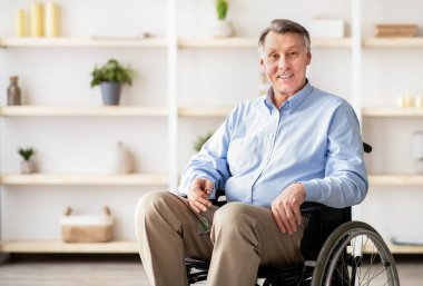 Tekerlekli sandalyedeki neşeli engelli adam huzurevinde gülümseyip kameraya bakıyor. Olumlu engelli yaşlı erkek portresi mutlu ve iyimser