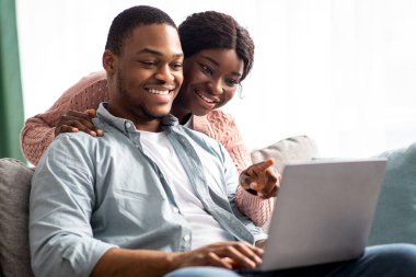 Evdeki kanepede dinlenirken dizüstü bilgisayar kullanan neşeli siyah çiftin yakın çekimleri. Birlikte komik içerikler izleyip, mekanı kopyalayacaklar. Afrika kökenli Amerikalı aile sevdalısı karı koca birlikte vakit geçiriyorlar.