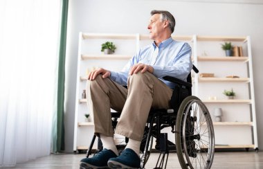 Düşük açılı tekerlekli sandalyedeki hasta pencereden dışarı bakıyor, evde üzgün ve çaresiz hissediyor. Kafkasyalı yaşlı bir adam engelli depresyonundan muzdarip, içeride.