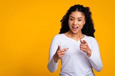 Hey sen! Neşeli genç siyahi bayan kamerayı işaret ediyor, Afro-Amerikalı olumlu kadın birini işaret ediyor, diyor ki, anladım, sarı arka planda tek başına duruyor, boşluğu kopyalıyor.