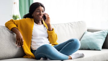 Neşeli, güzel, Afro-Amerikan genç bir kadın oturma odasında koltukta oturuyor, arkadaşlarıyla ya da ailesiyle cep telefonunda konuşuyor, fotokopi çekiyor. COVID-19 salgını sırasında iletişim