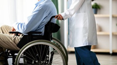 Tekerlekli sandalyedeki tanınmayan yaşlı erkek hasta ve huzurevindeki kadın bakıcısı. Kesik manzaralı. Hemşire engelli ihtiyarla ilgileniyor. Yaşlılar için tıbbi hizmetler