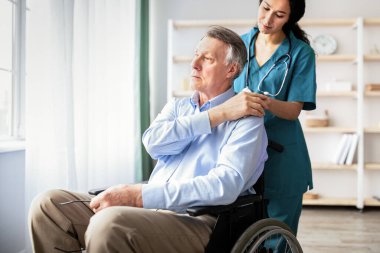 Genç doktor engelli erkeklerin elini tutuyor, huzurevinde ona destek oluyor. Tekerlekli sandalyedeki yaşlı adam depresyondan muzdarip. Milenyum hemşiresi ona içeride yardım ediyor.