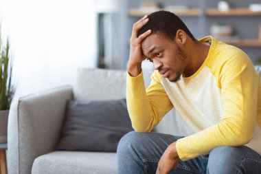 Hüsrana uğramış genç siyah adam oturma odasında koltukta oturuyor, alnına dokunuyor, maddi sıkıntılar yaşıyor ya da yalnızlık çekiyor, fotokopi odası, iç mekan.