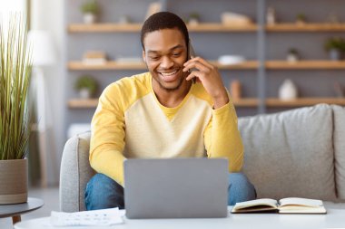 Akıllı telefondan konuşan gülümseyen siyahi adam, genç Afro-Amerikan iş adamı, evden internet üzerinden iş ortaklarıyla konuşuyor, uzaydan kopyalama yapıyor.