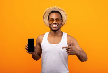 Yazlık kıyafetli siyahi adam sarı arka planda boş ekranlı cep telefonuna bakıyor. Cep telefonu uygulaması ya da web sitesi için boş yer var. Afro-Amerikalı adam reklamınız için akıllı telefon kullanıyor.