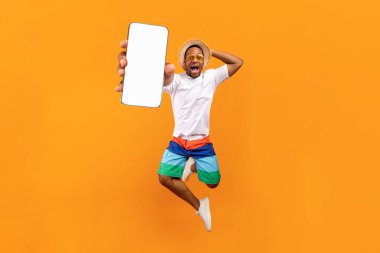 Güzel cep telefonu teklifi. Heyecanlı sıçrayan zenci adam turuncu arka planda beyaz ekranlı akıllı telefon gösterisi yapıyor uygulama veya web sitesi tasarımı için kopya alanı ile kolaj yapıyor.