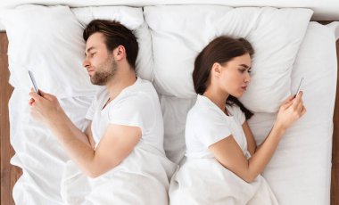 Evlilik krizi, kayıtsızlık. Birbirlerine kayıtsız bir şekilde yatakta sırt sırta uzanmış cep telefonu kullanan bir çift. Milenyum Eşleri Evde Sevgililerle Mesajlaşırken Birbirlerini Görmezden Geliyorlar. Yukarıdan Görüntüle