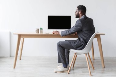 Afrika kökenli Amerikalı iş adamı masada oturuyor, bilgisayar ekranında web sitesi tasarımı için çalışıyor. Genç siyahi ofis çalışanı online ilanınız için fotokopi alanı teklif ediyor.