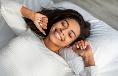 Sağlıklı Uyku, Uyku Hijyeni Konsepti. Çok güzel uyuyan Afro-Amerikan bir kadının yakın plan portresi. Evdeki yatakta uzanmış, kollarını kapalı gözlerle açmış, sabahları yatak odasında dinleniyor.