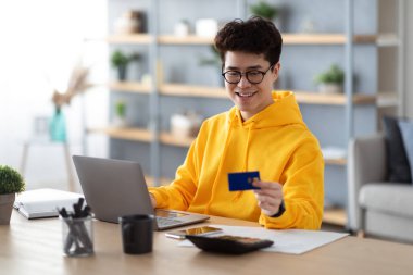 İnternetten alışveriş. Gözlüklü gülümseyen Asyalı bir adamın portresi PPC 'yi kullanarak masada oturuyor, kredi kartı alışverişine bakıyor, evdeki internet dükkanından para transfer ediyor. Omni Kanalı