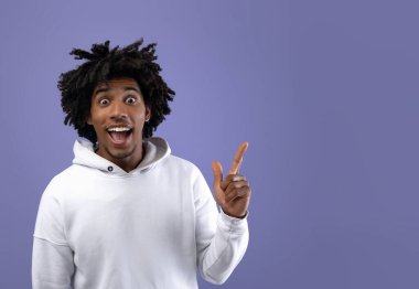 Çılgın siyahi genç adam AHA anı yaşıyor, yaratıcı bir fikri var, Violet stüdyosunun arka planına bakıyor, kopyalama alanı. Çekici Afro-Amerikan genci Eureka 'yı işaret ediyor.