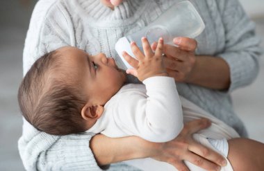 Bebek Bakımı ve Bebek Besleme Konsepti. Tanımlanamayan bir kadının elinde küçük tatlı bir Afrikalı Amerikalı bebeği tutması, elinde süt şişesi tutması, su içen çocuk.