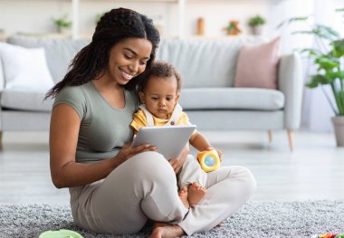 Leisure With Baby. Happy Black Mother And Cute Toddler Child Relaxing With Digital Tablet At Home, African American Mom And Kid Using Modern Gadget While Sitting Together On Floor In Living Room