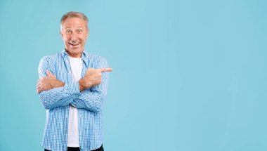 Özel bir teklif. Gülümseyen olgun bir adamın portresi mavi stüdyo arka planında izole bir şekilde duran bedava fotokopi alanını işaret ediyor. Heyecanlı erkek reklam ve panorama için boş maket mekanı gösteriyor
