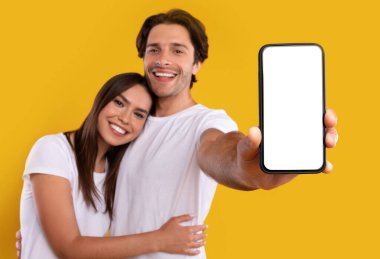 Cool Application kullanılıyor. Beyaz ekranlı akıllı telefonları olan sevimli bir çiftin portresi mobil uygulama öneriyor, web sitenizi tanıtıyor, sarılıyor, tasarım için makara yapıyor. Seçici odak