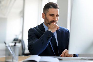 Bilgisayarla çalışan konsantre orta yaşlı erkek girişimci, ekrana bakıyor ve düşünüyor, ofis içinde çalışan odaklanmış iş adamı, serbest alan