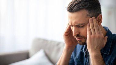 Evinde baş ağrısı çeken, şakaklarına dokunan, fotokopi çeken orta yaşlı sakallı bir adam. Migren, baş ağrısı, stres, gerilim sorunu, akşamdan kalma konsepti