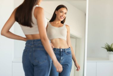 Çekici bir kadın, evde durup kilo verdikten sonra yansımasına bakarak gülümsüyor. Kendine güven kavramı. Seçici Odaklanma, Kırpılmış