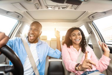 Yol Yolculuğu Konsepti. Heyecanlı Afro-Amerikan çiftin ön manzara portresi. Lüks araba sürüyorlar, müzik eşliğinde dans ediyorlar ve favori şarkılarını söylüyorlar, hafta sonları dinleniyorlar, tatile gidiyorlar, güneş parlıyor.