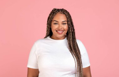 Kameraya gülümseyen mutlu Afrikalı Amerikalı kadın portresi artı beden tişört giyen ve stüdyoda pembe arka planda duran. Dişi Güzellik Konsepti