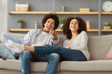 Evde akşam yemeği, komedi, covid-19 salgını. Binlerce yıllık Afro-Amerikan çifti rahat oturma odasında kanepede oturup uzaktan kumandalı televizyon izliyorlar.