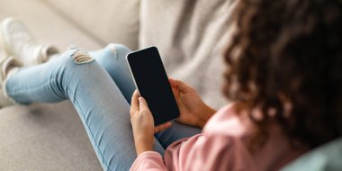 Tanımlanamayan kıvırcık siyah kız elinde siyah ekranlı akıllı bir telefon tutuyor, mobil uygulama kullanıyor ya da kullanışlı bir web sitesi kullanıyor. Model, kırpılmış, seçici odaklanma