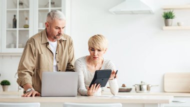 Hesaplarla, borçlarla ve ipoteklerle, mali zorluklarla ve vergilerle ilgili sorunlar. Ciddi üzgün, olgun Avrupalı erkek ve kadın, mutfak içi, boş uzay, dizüstü bilgisayar ve hesap makinesi ile masrafları göz önünde bulundururlar.