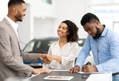 Araba almak. Satıcıyla tokalaşan siyah bir çift ve araba satış merkezinde imza dağıtan kağıtlar. Seçici Odaklanma