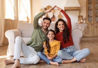 Bir aile yerde birlikte oturur, kolları ve elleriyle sembolik bir ev kurar, birlik olduklarını ifade ederler.