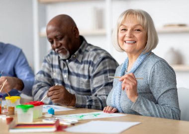 Yaşlılar için sanat terapisi. Yaşlılardan oluşan olumlu bir grup fırçayla resim yapmaktan, masanın etrafında oturmaktan, birlikte oturmaktan, destekli yaşam ve yakın çekim fotoğrafında iyi vakit geçirmekten hoşlanıyor.