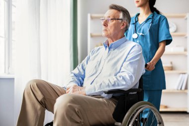 Genç hemşire, huzurevinde tekerlekli sandalyedeki engelli hastaya bakıyor. Yaşlılar yurdunda yetişkin engelli erkeklere yardım eden profesyonel bir tıbbi bakıcı.