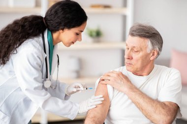 Genç doktor evdeki tekerlekli sandalyedeki engelli yaşlı adama ilaç ya da covid aşısı yapıyor. Sıhhiye bağışıklığı olan kıdemli engelli hasta, içeride antibiyotik iğnesi yapıyor.