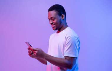 Sosyal ağdan mesajlar. Gülümseyen genç adam parlak akıllı telefona bak neon ışıkta, kopyala uzay