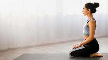Spor giyinen, evde yoga yapan, meditasyon yapan, fotokopi alanı olan, manzaralı, rahat genç bir kadın. Yoga, meditasyon, spor rutini, sağlıklı yaşam tarzı konsepti.
