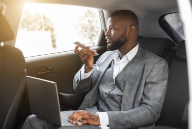 Genç siyah yönetici, lüks arabasıyla ofise giderken dizüstü bilgisayarda çalışıyor. Cep telefonuyla asistanına sesli mesaj kaydediyor. Arka koltukta oturuyor.