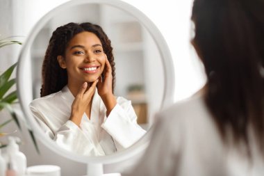 Cilt bakım konsepti. Aynaya Bakan ve Yüzüne Dokunan Güzel Siyah Kadın, Çekici Afrikalı Amerikalı Kadın Güzellik Tedavisinden Sonra Yumuşak Yumuşak Teni Hoşlanıyor, Seçici Odaklanma