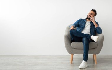 Akıllı telefondan konuşan, beyaz stüdyo duvarına karşı koltukta oturan mutlu genç bir Arap. Bin yıllık Orta Doğulu bir adam telefon ediyor, sohbet ediyor.