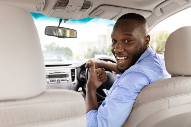 Harika araba. Mutlu Genç Siyah Adam İşaret İşaretini Gösteriyor, Yeni Otomobil Alma Mağazasında oturuyor, Tatilin tadını çıkarıyor, Yolcuya Bakıyor, Arka Koltuktan Bakıyor,