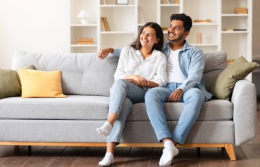 Neşeli Hintli çift, rahat rahat evlerinde bir kanepede oturuyorlar, bir ışık paylaşıyorlar, rüya gibi bir anı paylaşıyorlar, yandan seyrediyorlar ve şefkatli gülümsemeleri paylaşıyorlar, boş alanlar.