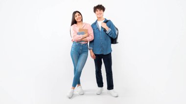 Eğitim Teklifi. Neşeli Genç Öğrenciler İkili Sırt çantaları ve çalışma kitaplarıyla beyaz arka planda duruyorlar. Üniversiteye hazır erkek arkadaş ve kız arkadaşın tam boy stüdyo çekimi. Panorama