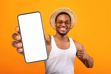 Yaz kıyafetleri içinde yakışıklı bir zenci elinde bira şişesi ve sarı stüdyo arka planında el kol hareketi yapıyor. Gülümseyen Afrikalı Amerikalı adam canlandırıcı alkollü içecek öneriyor.