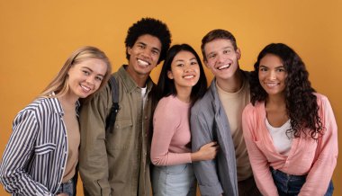 Göçmenlik ve yurtdışında eğitim, modern öğrenim ve takım çalışması. Mutlu genç çok ırklı öğrenciler eğleniyor, sarılıyor ve kameraya bakıyor, turuncu arka planda izole edilmiş, fotokopi alanı, stüdyo çekimi