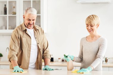 Evli çift evi temizliyor, tozunu alıyor, mobilyaların tozunu alıyor. Lastik eldivenler, süngerler, su püskürtücüler, fırçalar, mutfak içlerindeki dezenfekte masalarıyla neşeli bir aile çalışması.