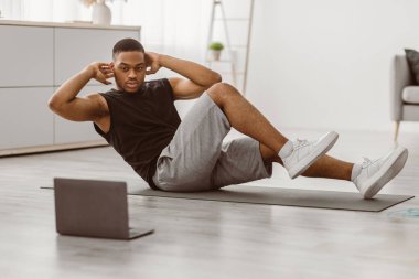 Sportif Afro-Amerikalı Adam, diz boyu dirsek, karın kaslarını çatlatıyor evde dizüstü bilgisayarda egzersiz yapıyor. Vücut geliştirme konsepti. Seçici Odaklanma