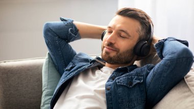 Rahatlama zamanı. Kablosuz kulaklıklı neşeli orta yaşlı adam müzik dinliyor, fotokopi çekiyor, yakın plan çekiyor. Kulaklık takmış, gözleri kapalı, oturma odasında kanepede dinlenen mutlu, yakışıklı bir adam.