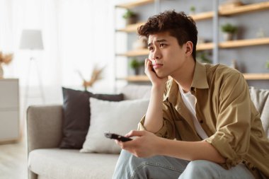 Sıkıcı Televizyon Programı. Sıkıcı Asyalı adam TV izliyor uzaktan kumandayla kanal değiştiriyor evdeki koltukta oturuyor. Hoşnutsuz İzleyici İlginç Olmayan Film İzliyor, Yalnız Hissediyor