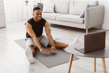 Evde antrenman. Spor Siyah Adam Laptop Bilgisayar 'da egzersiz yapıyor. Oturma odasında Mat Eğitiminde Oturan Çevrimiçi Spor Konferansı' nı izliyor. Spor Yaşam Tarzı. Seçici Odaklanma