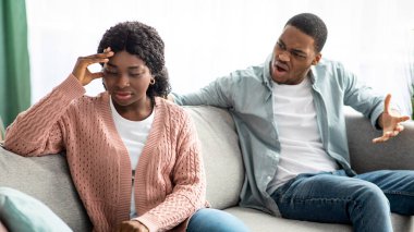 Kızgın siyah adam üzgün kız arkadaşına bağırıyor, evdeki oturma odasında kanepede oturuyor. Genç Afro-Amerikan çifti kavga ediyor, ilişki ya da evlilik krizi yaşarken salgın sırasında