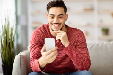 Olumlu Arap adam evde yepyeni bir cep telefonu kullanıyor, arkadaşlarıyla online parti veriyor, telekomünikasyon için güzel bir uygulama kullanıyor. Akıllı telefon tutan mutlu orta doğulu adam, kopyala uzay